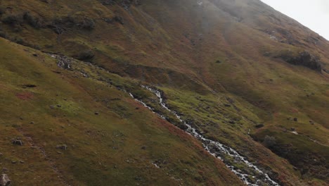 Dramatic-turn-along-a-Scottish-hillside-to-center-on-a-stream-of-mountain-water-rushing-downhill-in-the-Glencoe-region-of-Scotland