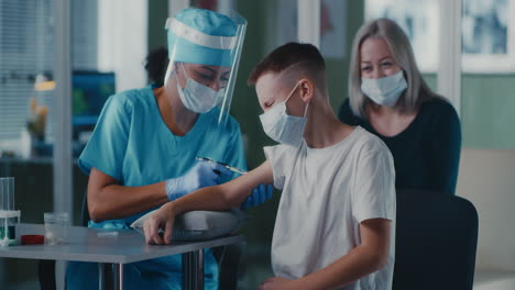 a young boy receives a vaccine shot from a nurse while his mother watches