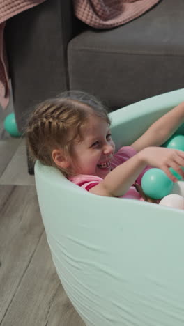 joyful little children have fun in dry pool with colorful balls in living room. cute blond brother and elder blonde sister play together at home