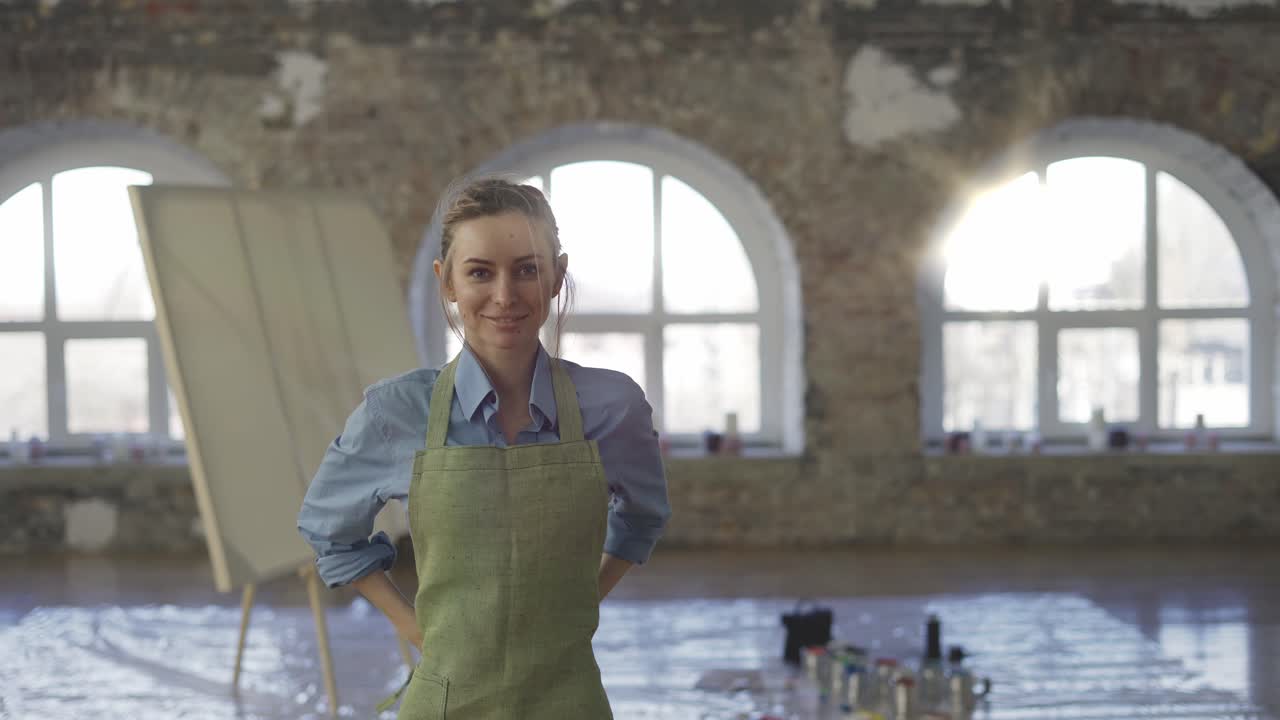Porträt einer Frau, die eine Schürze anzieht, um in einer großen Werkstatt mit dem Malen zu beginnen.