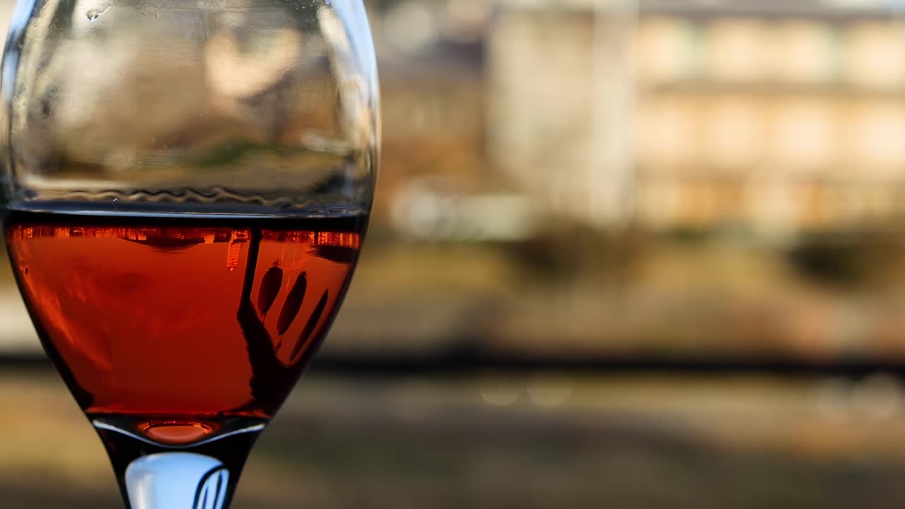A detailed view of a wine glass filled with red liquid against a blurred urban background.