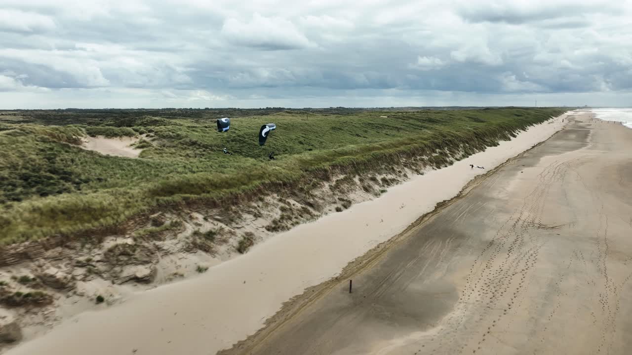 hermoso dron aéreo cinematográfico cerca de dos personas volando en parapente cerca del borde del agua en una playa en holanda