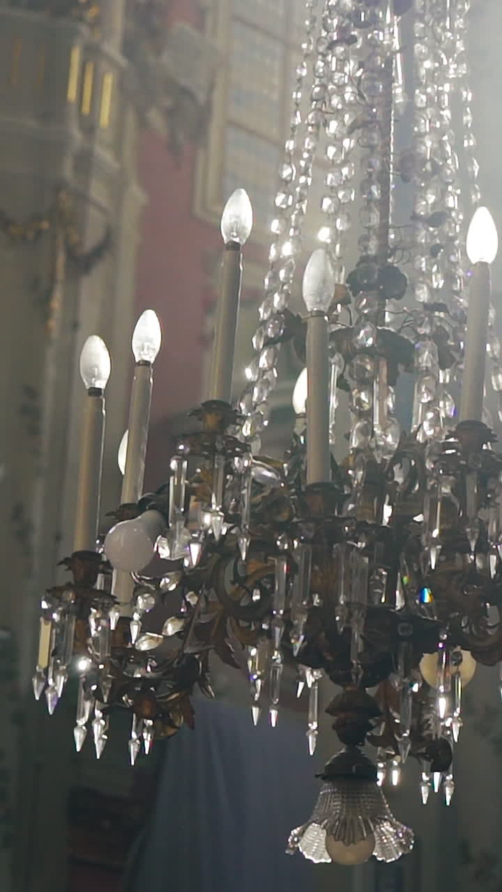 a luxurious chandelier hangs in the middle of a catholic cathedral on the background of frescoes. Camera motion to the side. Vertical video