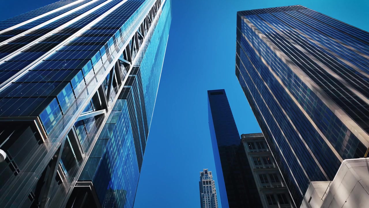 Opwaartse opname tussen moderne glazen wolkenkrabbers in Midtown Manhattan, met de nadruk op reflecterende gevels, torenhoge architectuur en een helderblauwe zomerhemel in New York City