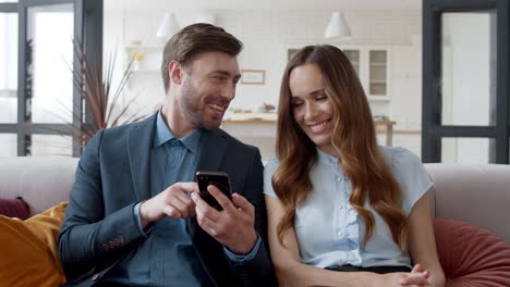 Pareja-Sonriente-Mirando-Teléfono-Móvil-En-La-Oficina-Del-Hogar.-Hombre-Y-Mujer-Riendo.