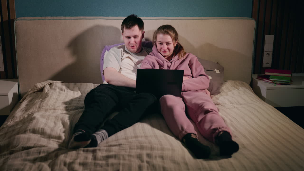 una pareja relajándose en la cama viendo una computadora portátil.