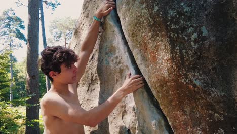 close up of young muscular man climbing crag boulder shirtless in fontainebleau