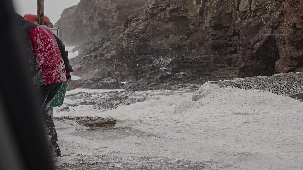 Femme couverte de neige comme de l'écume de mer pendant la tempête hivernale extrême Eunice sur la côte de la plage de Chapel Porth en Cornouailles, Royaume-Uni