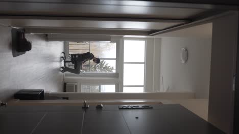 vertical video, young man with laptop and headphones sitting in chair in bright room, listening music online, static, open door view