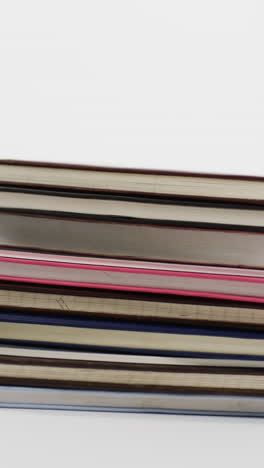 vertical video of stack of books with copy space on grey background, in slow motion