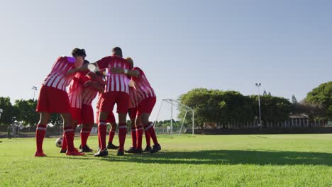 video of diverse group of male football players on field,discussing game tactics