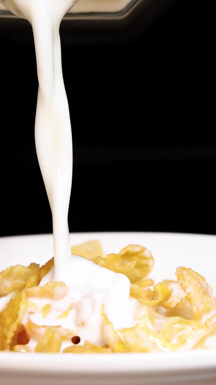 Il latte scende a cascata in una ciotola di cereali di mais su uno sfondo nero, creando una scena dinamica per la colazione.