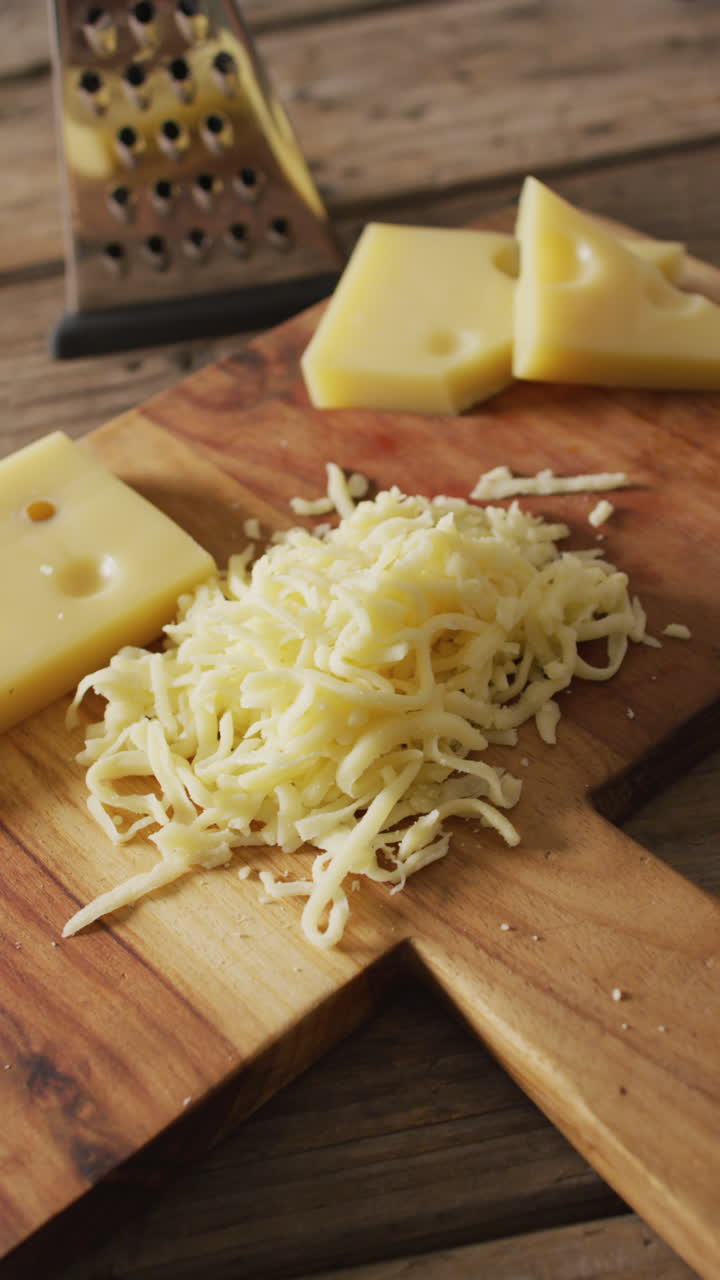 video vertical de queso rallado y pedazos de queso con rallador en tabla de madera