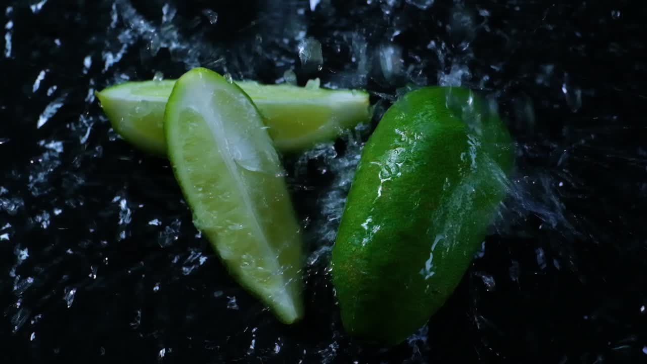 어두운 작업 표면에서 슬로우 모션으로 세탁되는 슬라이스 된 라임의 영화 영상, 슬로모