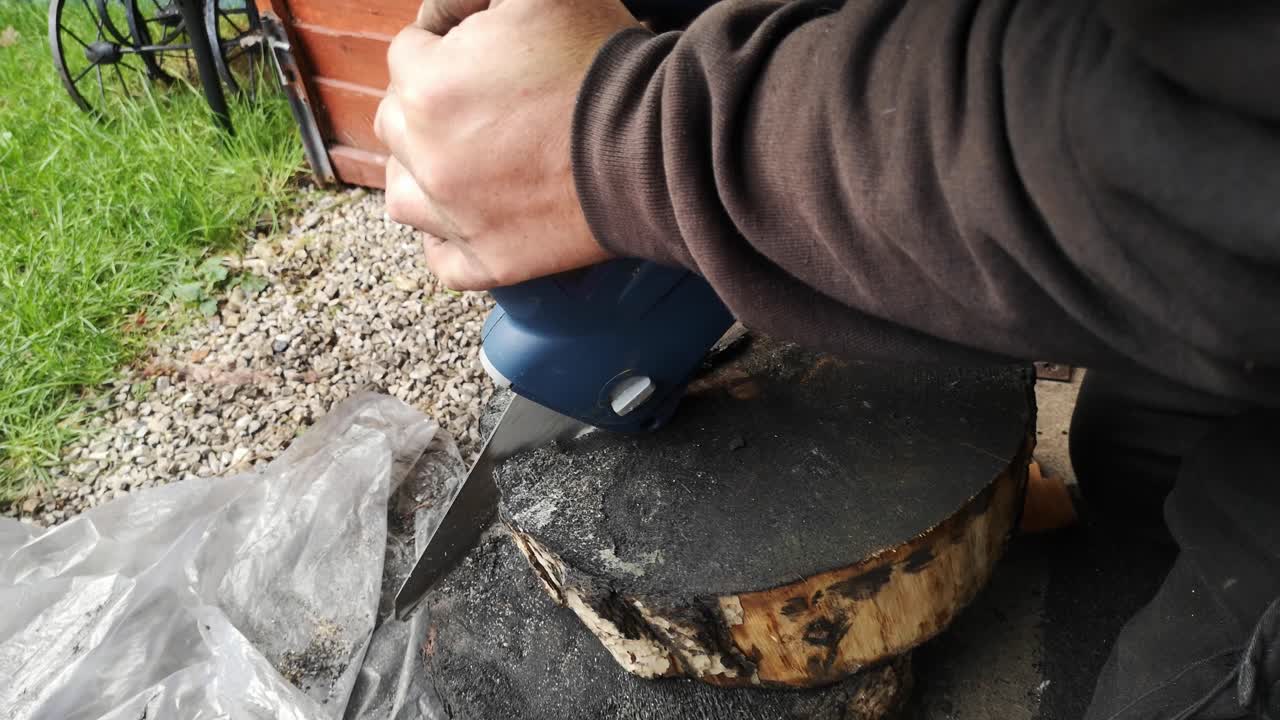 hombre molesto que lucha para cortar rodajas de leña quemada con sierra eléctrica