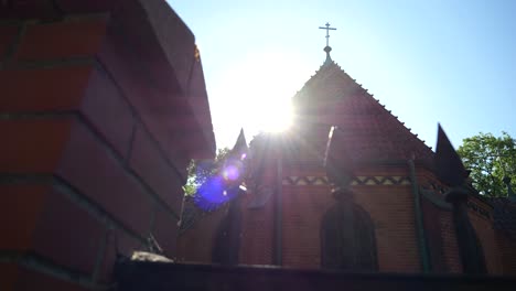 Cross-on-the-rooftop-of-a-church,-seen-in-full-sunlight-from-behind-a-fence