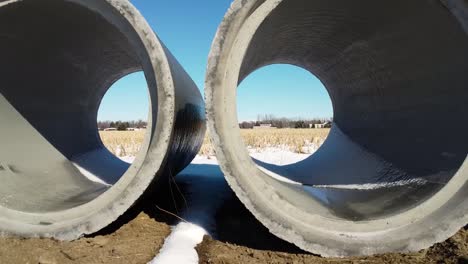 moving drone shot looking though concrete pipes at snow covered wheat field