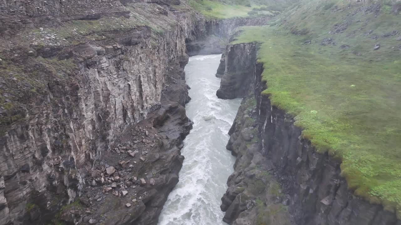 A powerful whitewater river flows through a deep, rocky canyon with green banks.