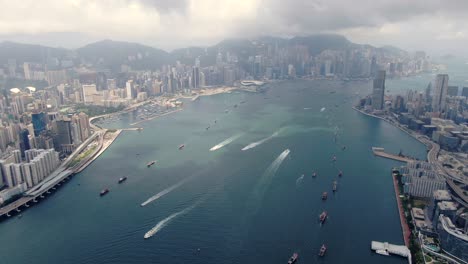 Convoy-of-local-Fishing-boats-causing-in-Hong-Kong-Victoria-bay,-with-city-skyline-in-the-horizon,-Aerial-view