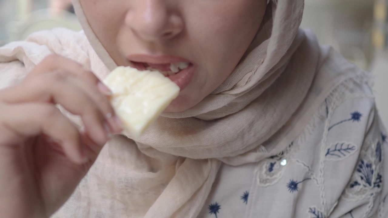 Woman Wearing Hijab Eating a Piece of Cheese