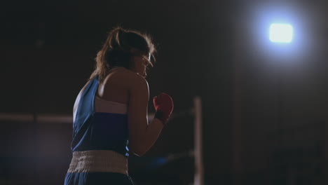 A-beautiful-woman-conducts-a-shadow-fight-practicing-technique-and-speed-of-strikes-while-training-hard-for-future-victories.-Dark-gym-background.-steadicam-shot