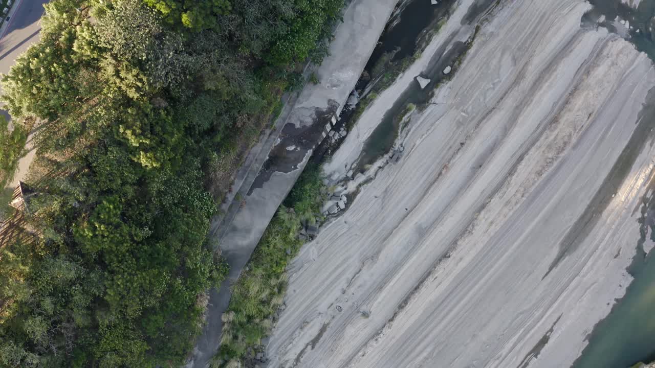 Aerial shot of rocky seaside cliffs, lush green trees, and park pathways under sunlight. Perfect for nature, travel, or environmental stock footage in 4K