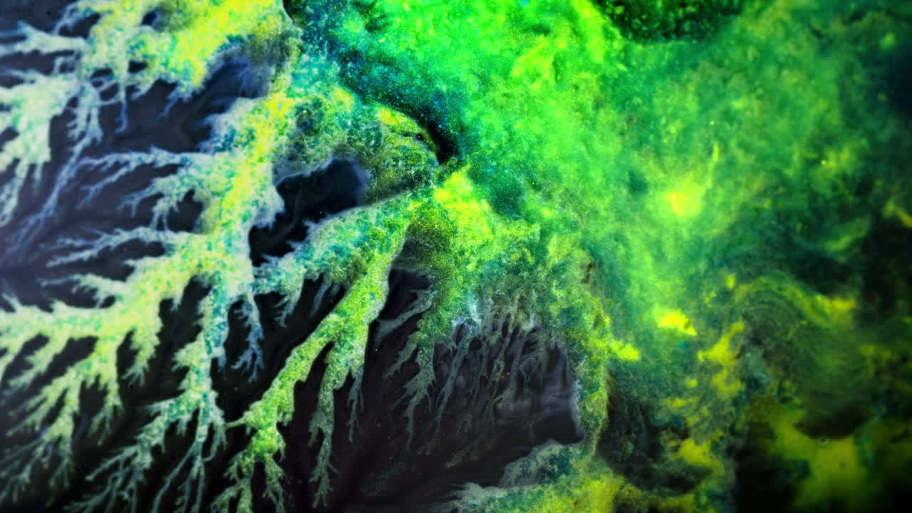 Colorful ink blending into water with vibrant green and yellow hues, macro shot