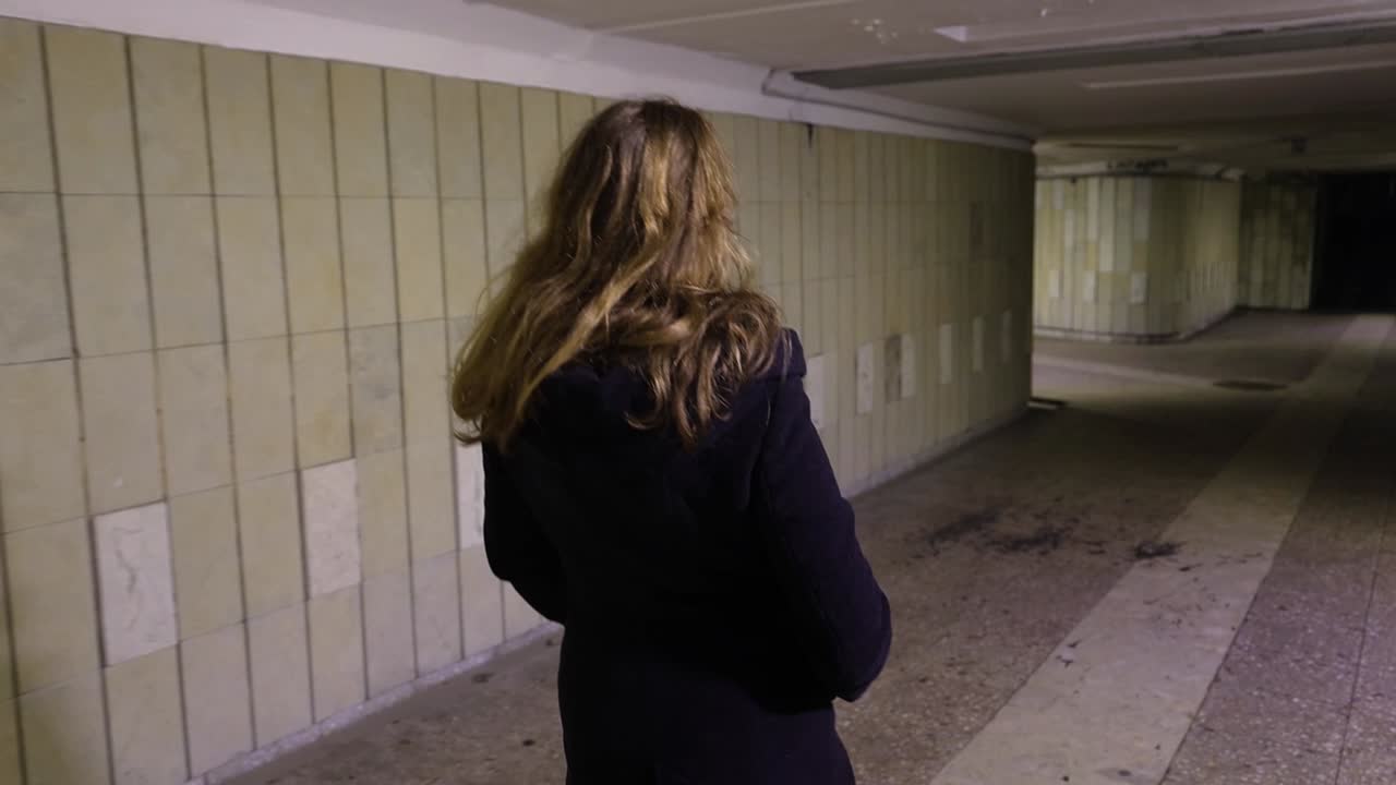 Girl walking in the underground passage at night, view from the back