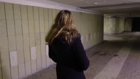 girl walking in the underground passage at night, view from the back