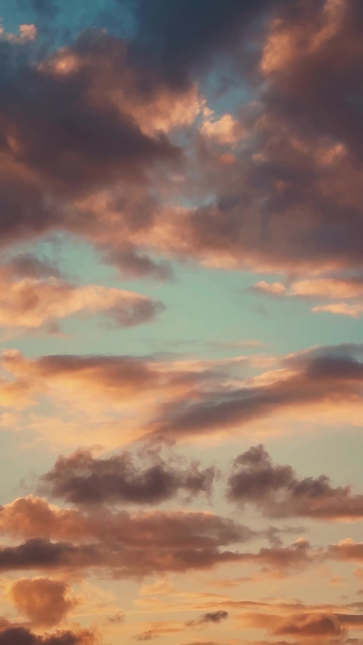Warm golden light illuminates drifting clouds moving gently across a calm blue sky, captured in a vertical cinematic style. Vertical video, ideal for social media.