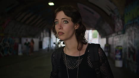 anxious young alternative style woman walking along dark underpass with graffiti covered walls on london city street uk in real time 1