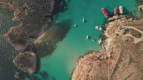 aerial overhead zoom out and follow drone shot of a boat leaving malta's magnificient blue lagoon, renowned for its crystal-clear waters