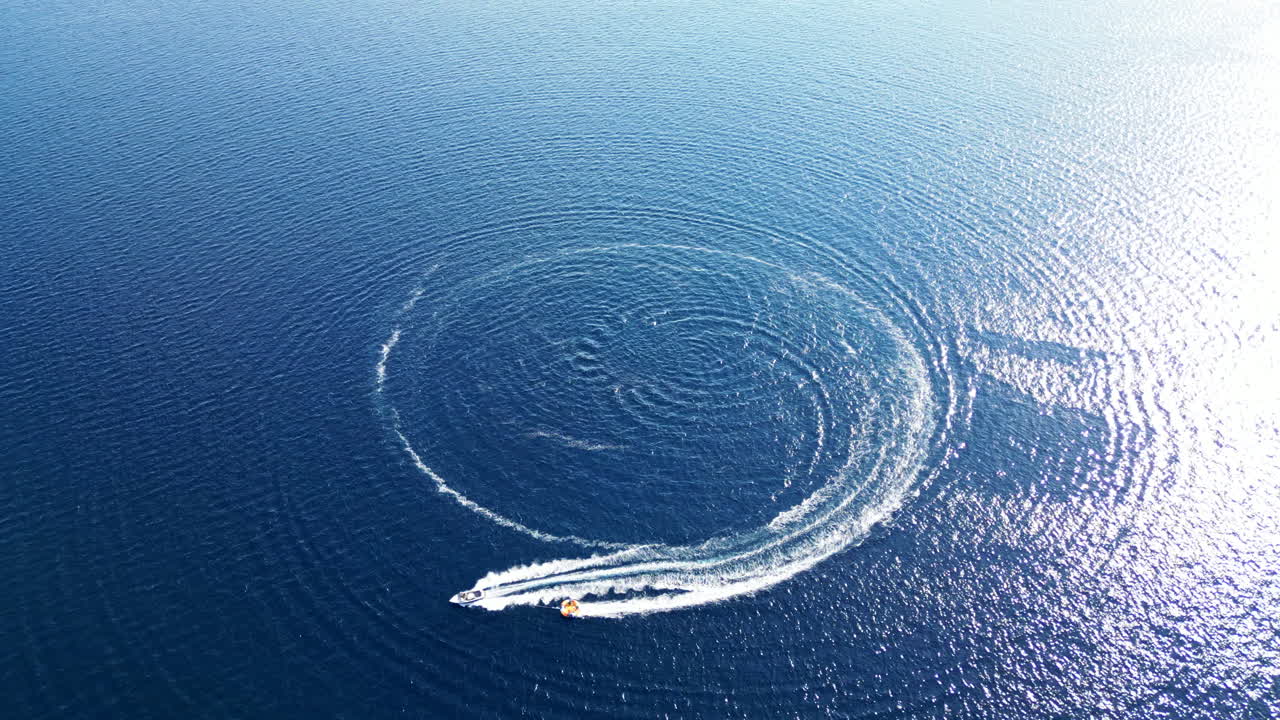 Motorboat making circles on a deep blue water surface leaving a white foamy trail. Drone flying away. Croatia