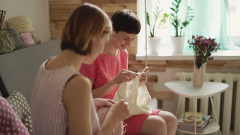 Knitting-woman-friends-sitting-talking-on-couch-in-room-on-background-window