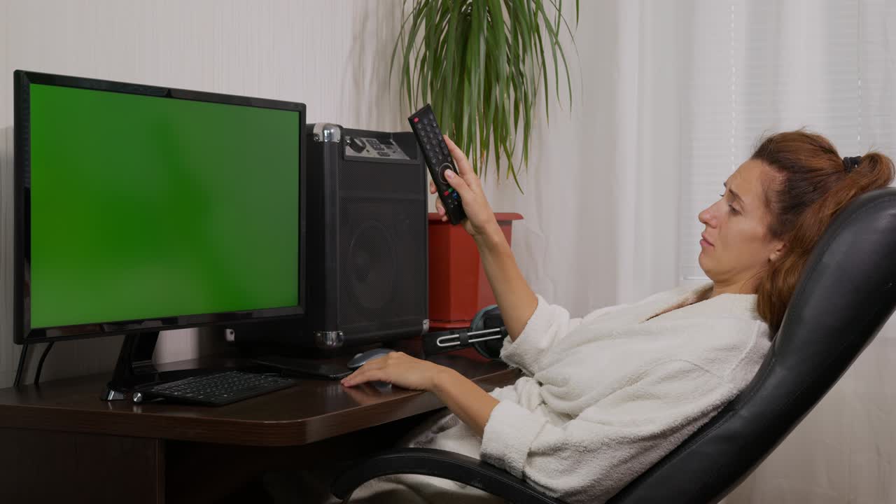 una mujer está viendo la televisión con una pantalla verde. cambia de canal con el control remoto.