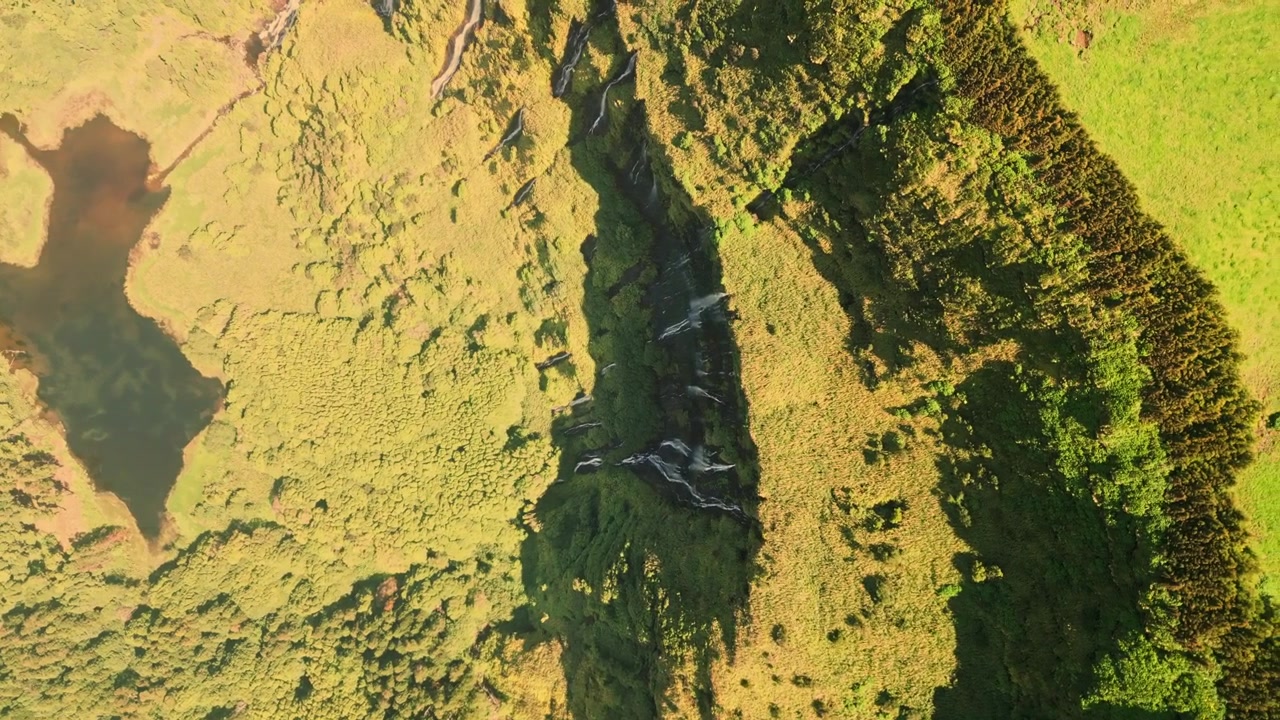 Luftfoto bevæger sig over frodigt grønt landskab med vandfald og en lille sø, Flores.
