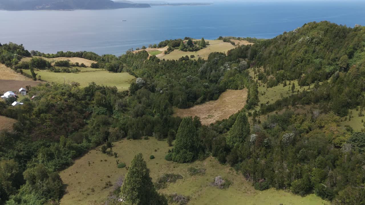 Aerial view of the landscape of Lemuy Island, part of the Chiloe archipelago, Chile, showing the fields, forest and the Pacific Ocean. push forward,tilt up shot