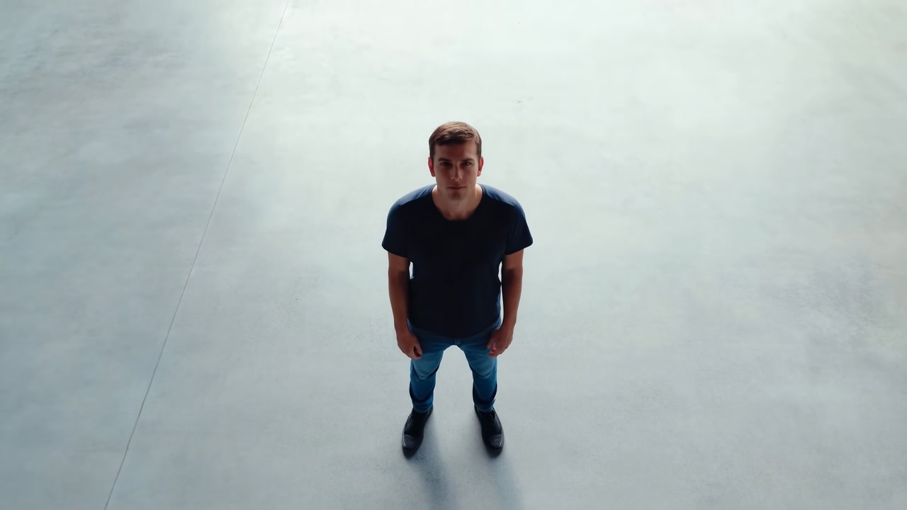 Young White Man Standing On Concrete Floor Looking Up, Hands In Pockets, Wearing Dark Shirt And Jeans,