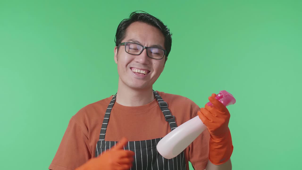 손에 스프레이를 들고 있는 아시안 남성 하녀의 클로즈업 사진. 그 다음에는 그린 스크린 스튜디오에서 카메라를 향해 엄지손가락을 보여준다.