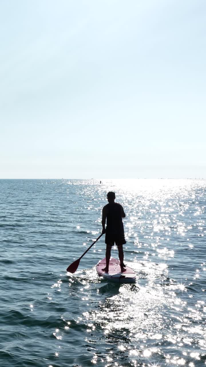 Paddle surfer gliding on calm ocean water. Vertical