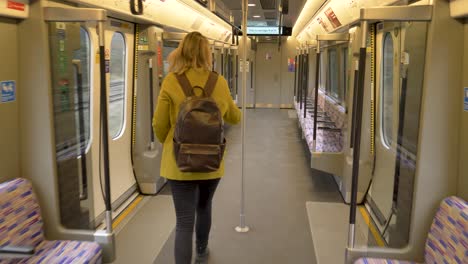 Müde,-Erschöpfte,-Beschäftigte-Frau-Mit-Einem-Schweren-Rucksack,-Die-Einen-Leeren-U-Bahn-Wagen-Entlangläuft-Und-Alleine-Platz-Nimmt