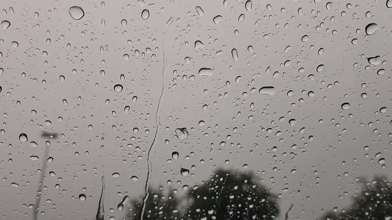 This is a short video clip of rain, falling onto a car window, creating large droplets and small streams of water, flowing down the window