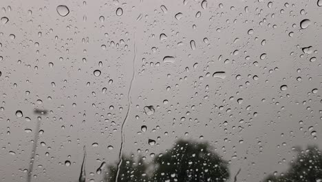 this is a short video clip of rain, falling onto a car window, creating large droplets and small streams of water, flowing down the window