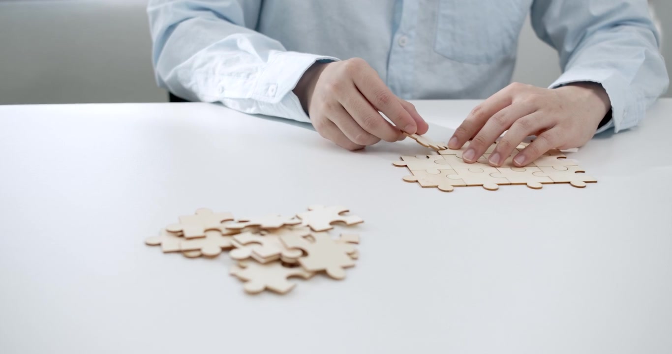 Mani di un professionista d'affari che lavora su un puzzle di legno, riflettendo concetti di lavoro di squadra, pianificazione strategica e raggiungimento degli obiettivi aziendali con cooperazione e unità.