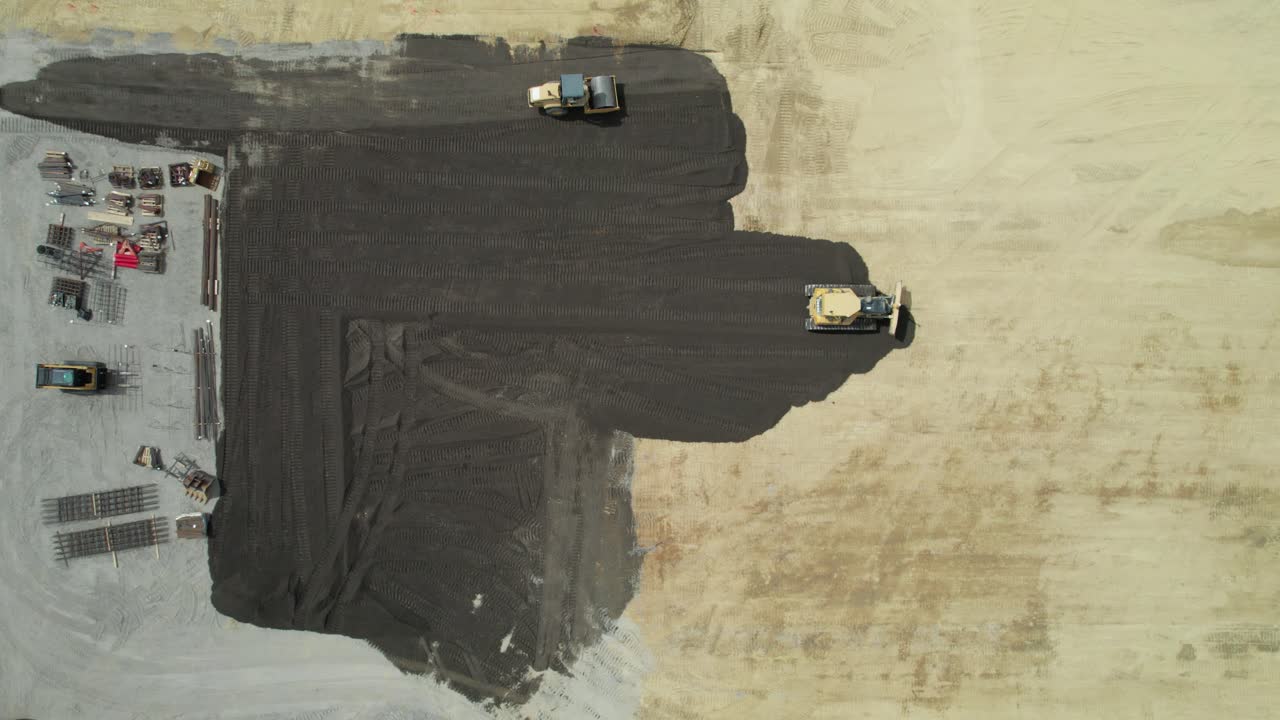 Aerial view of yellow tracked tractor rakes the ground to build an asphalt road