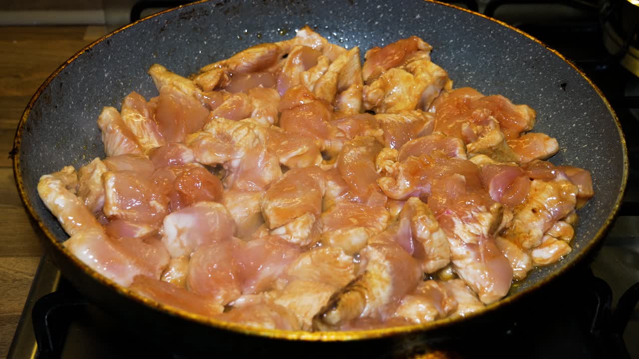 las rodajas de pollo se cocinan en una sartén caliente con burbujas de aceite y vapor blanco.