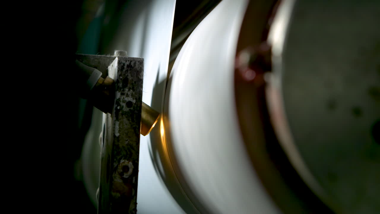 Closeup of a spinning metal roll and a small spotlight shining on printed wallpaper rolling by