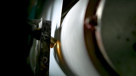 closeup of a spinning metal roll and a small spotlight shining on printed wallpaper rolling by