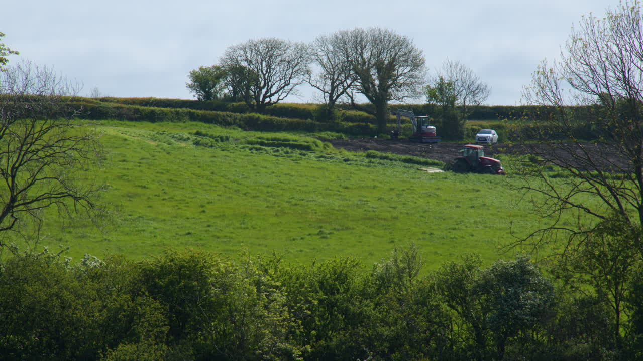 Distant longshot of tractor in field with JCB working in background