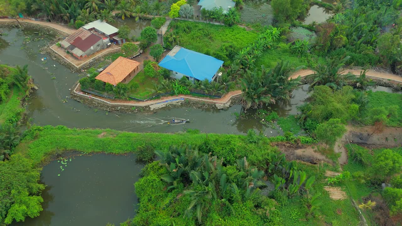 Aerial drone view of peaceful countryside showing rural homes beside winding river and dense green vegetation, with tropical trees, ponds, and scattered houses in tranquil natural setting